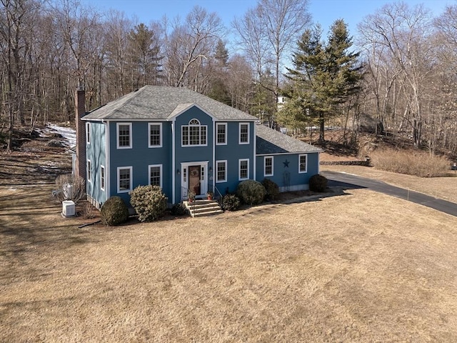 view of front of home with a front lawn, a shingled roof, and cooling unit