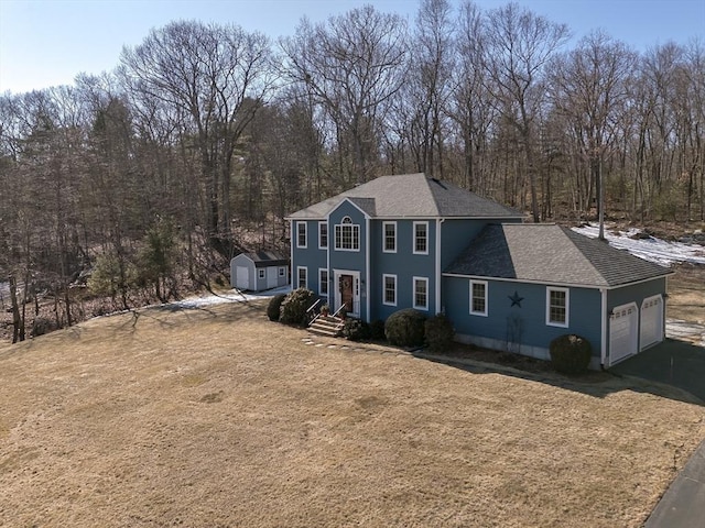 colonial inspired home featuring a shingled roof, a front yard, driveway, and an attached garage