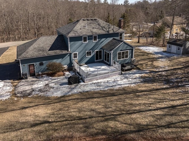 back of property with a deck, driveway, a chimney, and a view of trees