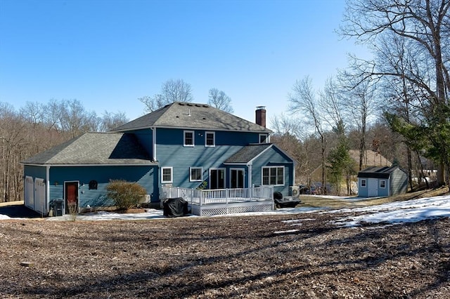 rear view of house featuring a deck, an attached garage, an outdoor structure, a shed, and a chimney