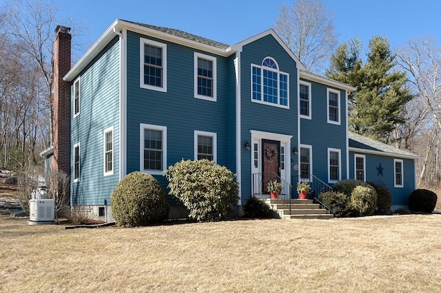 colonial house with a chimney, cooling unit, and a front yard