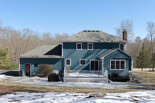 snow covered back of property with a deck, ac unit, and a chimney