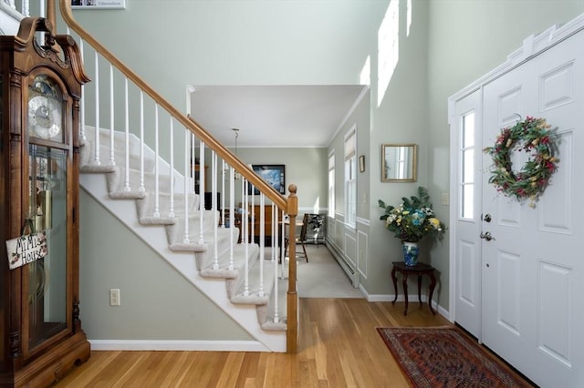 entryway featuring baseboards, a towering ceiling, ornamental molding, stairs, and light wood-type flooring