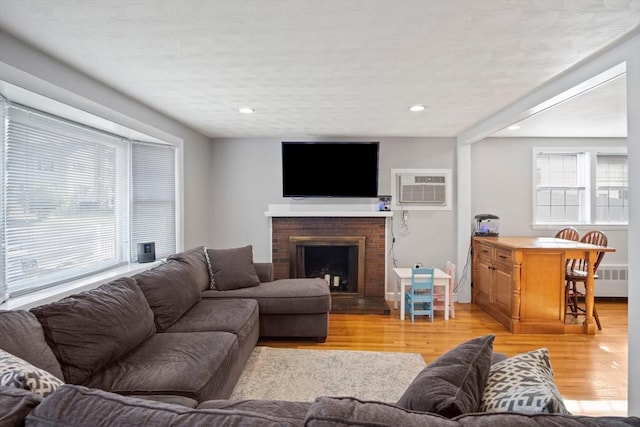 living room with a wall mounted air conditioner, light wood-type flooring, radiator, a fireplace, and recessed lighting