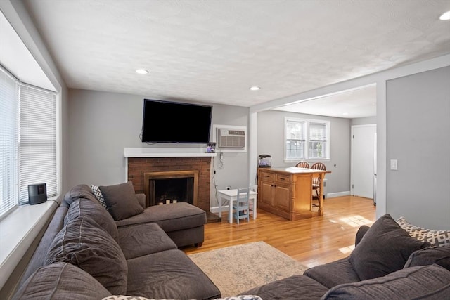 living room with a wall mounted air conditioner, recessed lighting, light wood-style flooring, and a fireplace