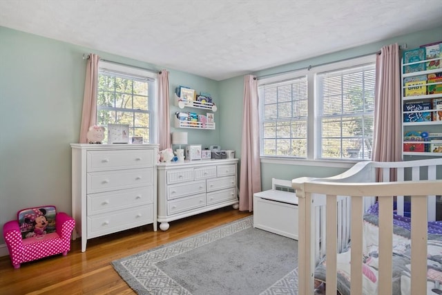 bedroom with wood finished floors, multiple windows, a textured ceiling, and a nursery area