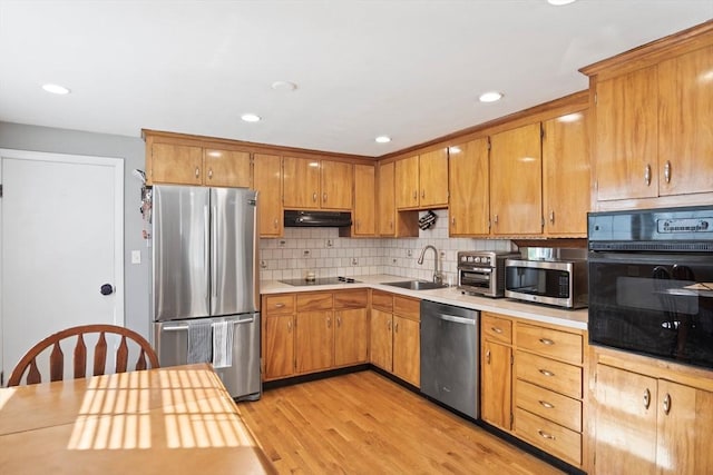 kitchen featuring black appliances, a sink, under cabinet range hood, light countertops, and light wood-type flooring