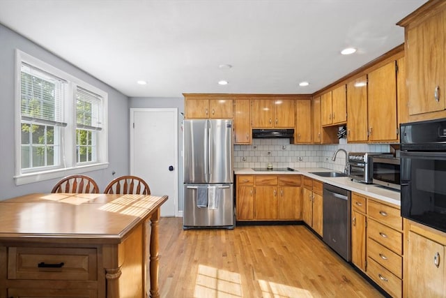 kitchen featuring black appliances, light wood-type flooring, under cabinet range hood, a sink, and brown cabinets