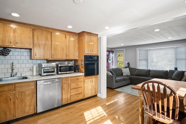 kitchen with appliances with stainless steel finishes, a sink, light countertops, light wood-style flooring, and tasteful backsplash
