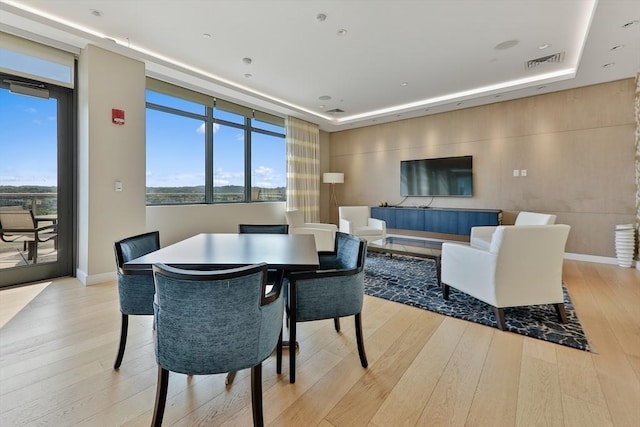 dining space with a tray ceiling, visible vents, wood finished floors, a wall of windows, and baseboards