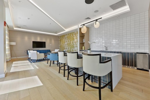 bar with light wood-type flooring, a tray ceiling, visible vents, and backsplash