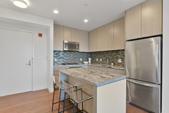 kitchen featuring a breakfast bar, appliances with stainless steel finishes, a center island, light brown cabinetry, and light wood finished floors