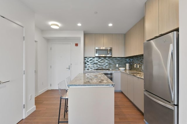 kitchen featuring light wood-style flooring, appliances with stainless steel finishes, tasteful backsplash, and a center island