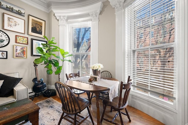 dining area featuring baseboards, crown molding, decorative columns, and wood finished floors