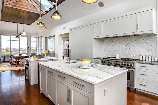 kitchen with light stone countertops, stainless steel stove, pendant lighting, a kitchen island with sink, and sink