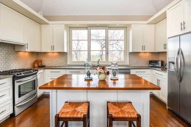 kitchen with white cabinets, appliances with stainless steel finishes, wood counters, and a breakfast bar area