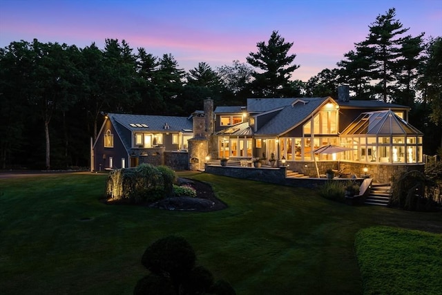70 Lazell St, Hingham, MA 02043 - back of property at dusk with a chimney, stone siding, and a lawn