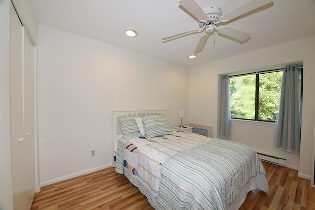 bedroom featuring hardwood / wood-style flooring, ceiling fan, baseboard heating, and a closet