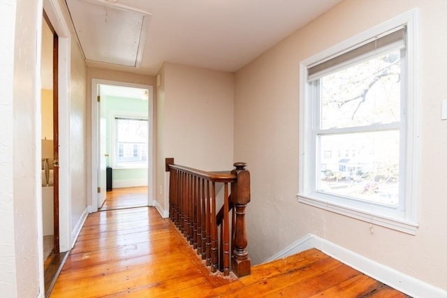 corridor featuring baseboards, attic access, light wood finished floors, and an upstairs landing
