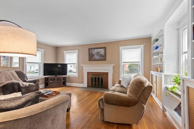 living area with crown molding, wood-type flooring, a healthy amount of sunlight, and a fireplace