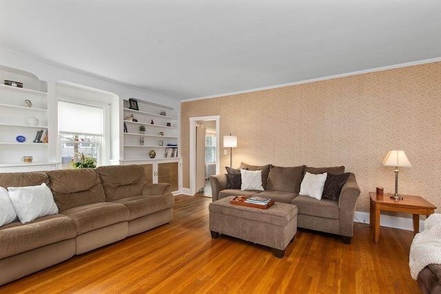 living room featuring built in features, ornamental molding, wallpapered walls, and wood finished floors