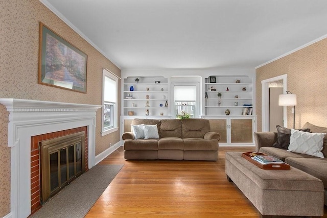 living area with crown molding, built in features, a brick fireplace, light wood-style floors, and wallpapered walls
