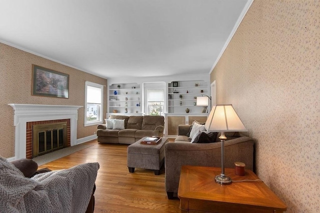 living area with a brick fireplace, wallpapered walls, ornamental molding, and light wood-style flooring