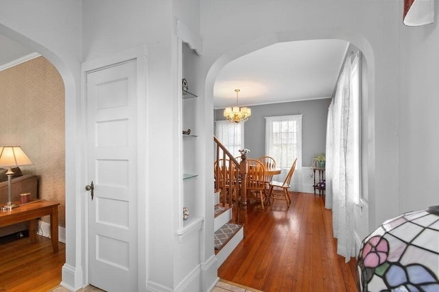 hall featuring crown molding, arched walkways, hardwood / wood-style flooring, built in shelves, and a chandelier