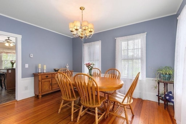 dining room featuring crown molding, wainscoting, ceiling fan with notable chandelier, and hardwood / wood-style flooring