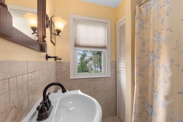 full bath with a sink, a shower with shower curtain, a wainscoted wall, and tile walls