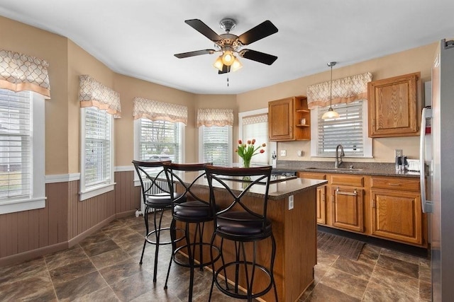 kitchen featuring a kitchen island, brown cabinets, a sink, a wainscoted wall, and a breakfast bar