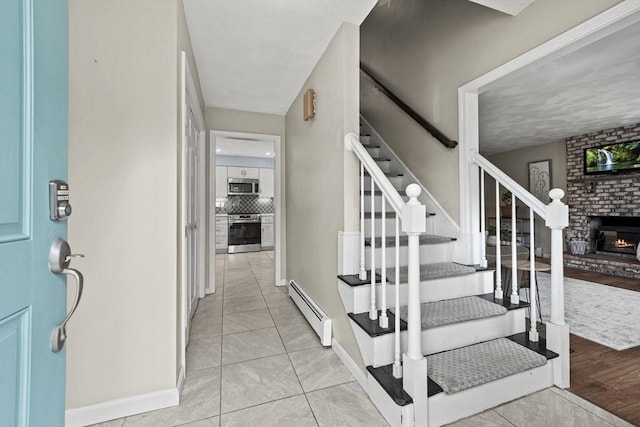 stairway featuring tile patterned flooring, a fireplace, a baseboard heating unit, and baseboards