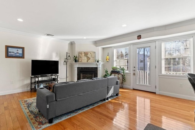 living room featuring a high end fireplace, ornamental molding, and light hardwood / wood-style flooring