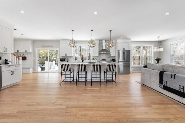 57 Chittenden Rd, Scituate, MA 02066 - kitchen featuring wall chimney exhaust hood, freestanding refrigerator, a kitchen breakfast bar, light wood-style floors, and white cabinets