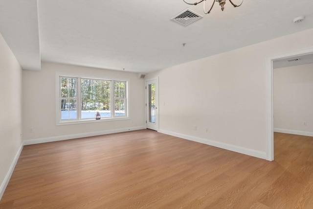 spare room featuring a notable chandelier, light wood-style flooring, visible vents, and baseboards