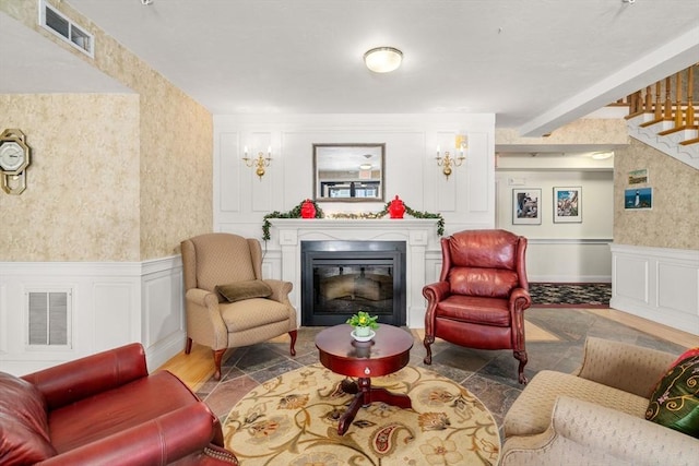 sitting room with a glass covered fireplace, visible vents, a decorative wall, and wallpapered walls