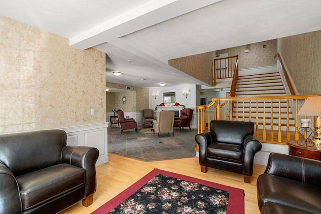 living room featuring a decorative wall, wood finished floors, stairway, wainscoting, and wallpapered walls