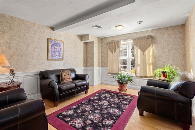 living room featuring wallpapered walls, light wood finished floors, and a wainscoted wall