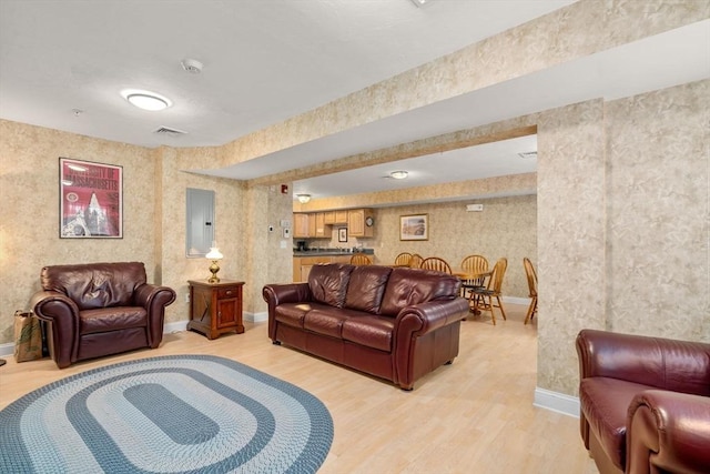 living area with visible vents, light wood-style floors, electric panel, baseboards, and wallpapered walls