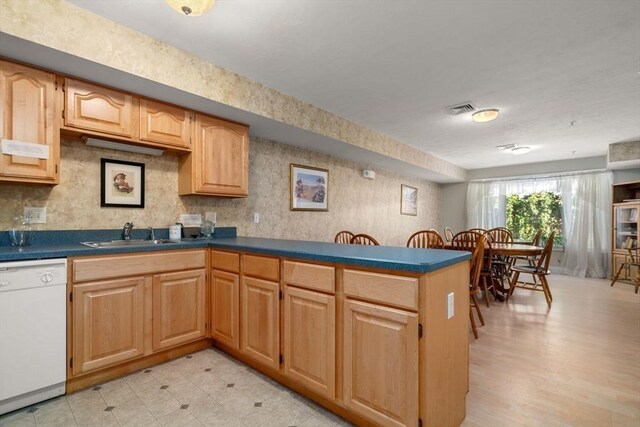 kitchen featuring white dishwasher, a sink, visible vents, light floors, and dark countertops