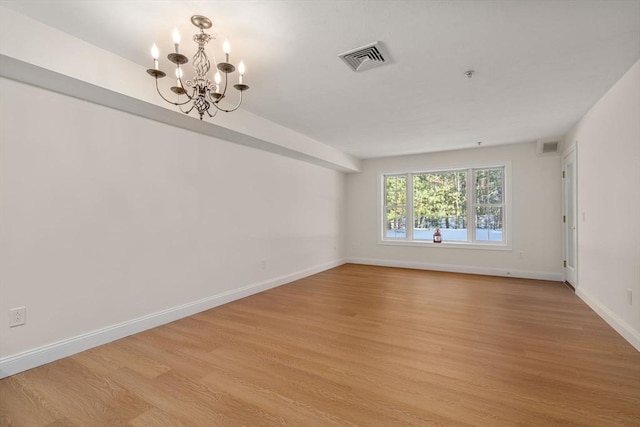 spare room with baseboards, light wood-type flooring, visible vents, and an inviting chandelier