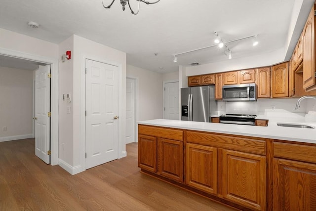 kitchen featuring stainless steel appliances, a peninsula, a sink, light countertops, and brown cabinets