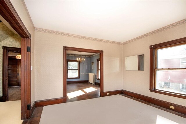 unfurnished bedroom with baseboards, a notable chandelier, wood finished floors, and wallpapered walls