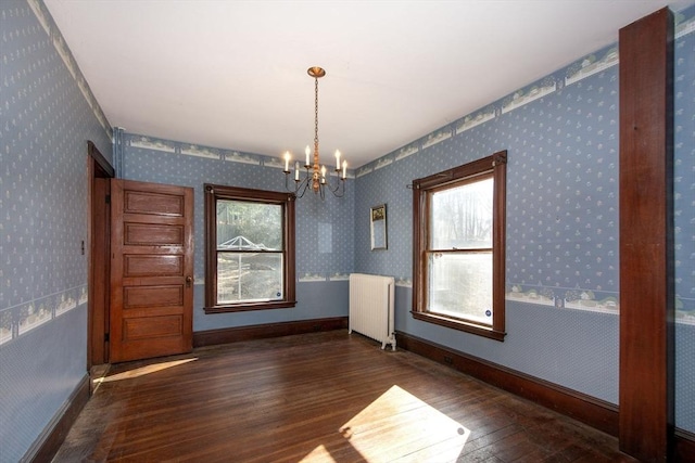 unfurnished room with wallpapered walls, baseboards, radiator heating unit, an inviting chandelier, and wood finished floors