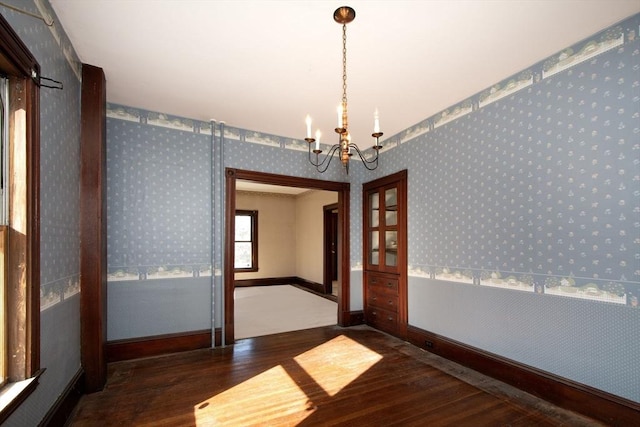 spare room featuring a notable chandelier, wallpapered walls, baseboards, and wood finished floors