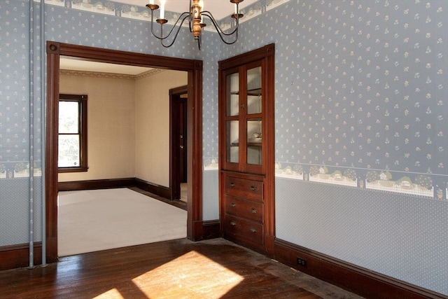 unfurnished room with baseboards, a notable chandelier, wood finished floors, and wallpapered walls