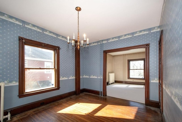 unfurnished room with wood finished floors, radiator, an inviting chandelier, wallpapered walls, and baseboards