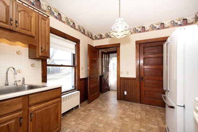 kitchen featuring radiator, wallpapered walls, a wainscoted wall, freestanding refrigerator, and a sink