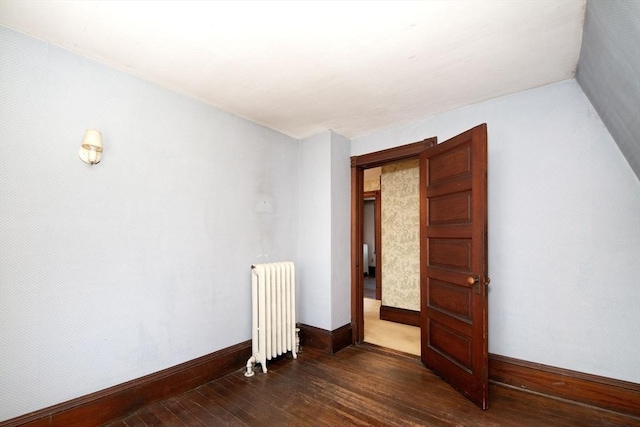 unfurnished room with dark wood-style floors, radiator, and baseboards