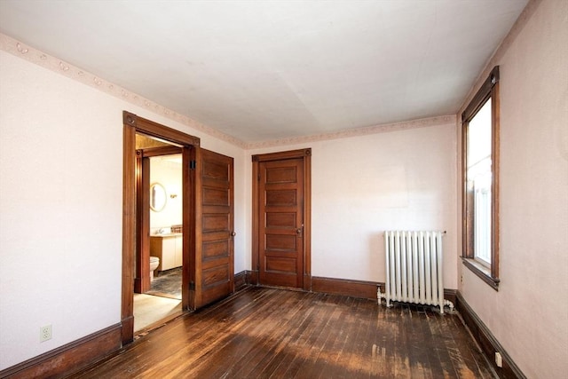 empty room with baseboards, radiator, a healthy amount of sunlight, and dark wood-style floors